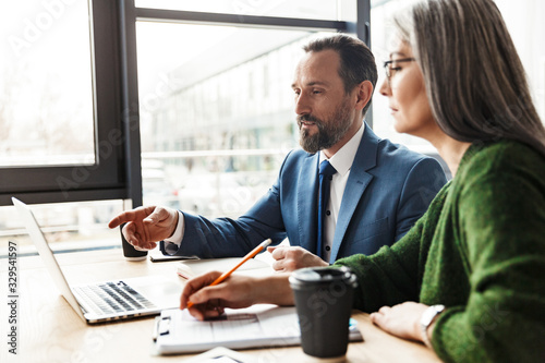 Photo of colleagues talking while working with laptop and documents