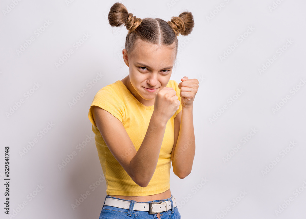 Funny angry teen girl standing up and preparing to fight, on gray background. Child looking confident at camera. Strong and aggressive teenager with fists in boxing pose. Funny angry teen girl standing up and preparing to fight, on gray background. Child looking confident at camera. Strong and aggressive teenager with fists in boxing pose.