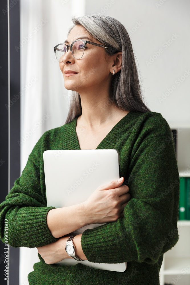 Photo of gray-haired serious businesswoman holding laptop Photo of gray-haired serious businesswoman holding laptop
