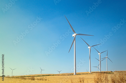Windmills wind turbines farm power generators against landscape against blue sky in beautiful nature landscape for production of renewable green energy. Friendly industry to environment.