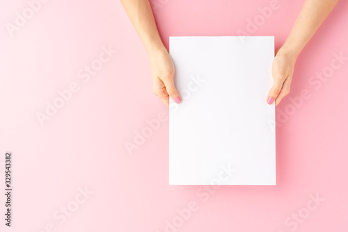 Female hands holding blank white paper sheet on pink background. Mock up