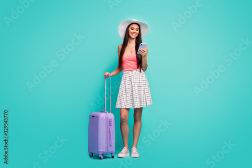 Full length photo positive girl arrive summer weekend resort use smartphone search book hotels hold trolley wear sunhat pink singlet white checkered plaid skirt isolated teal color background