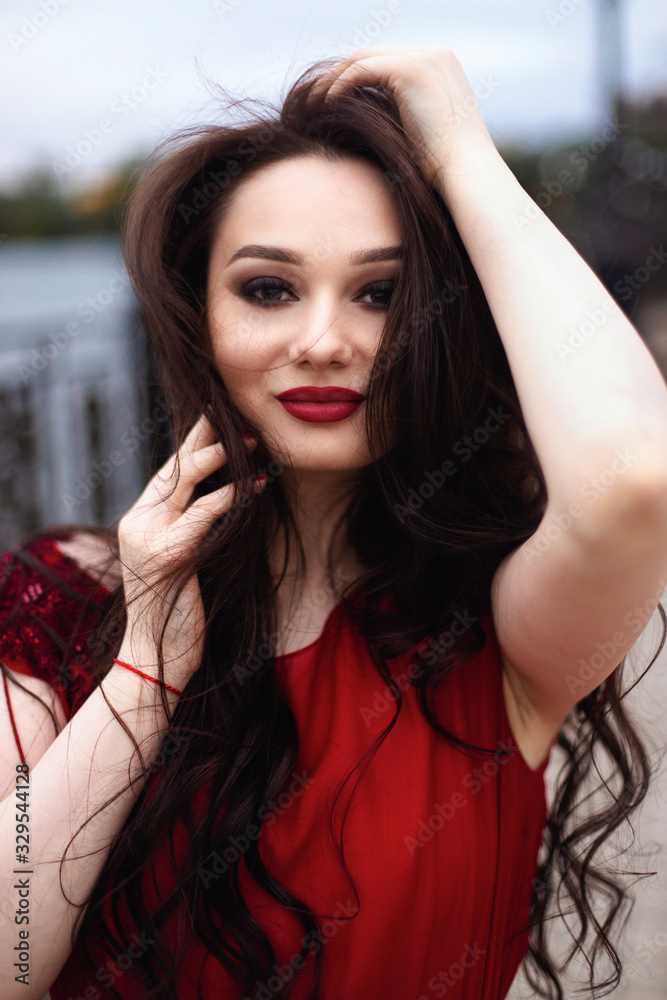 Portrait of a young brunette woman in a red dress with a train