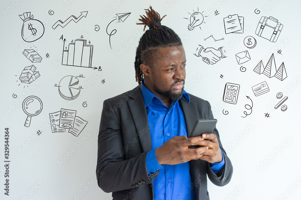 African man texting message with hand drawn business sketches. Concentrated hipster young businessman with smartphone looking away. Pensive handsome black male manager using gadget. Mobility concept