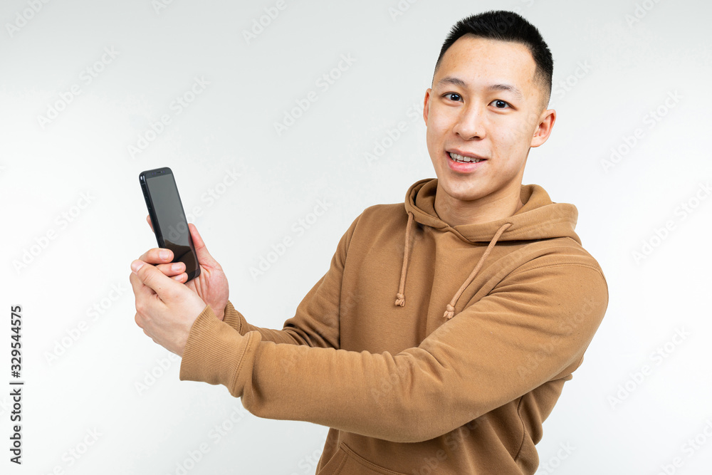 Asian guy shows a smartphone in his hand on a white background Asian guy shows a smartphone in his hand on a white background