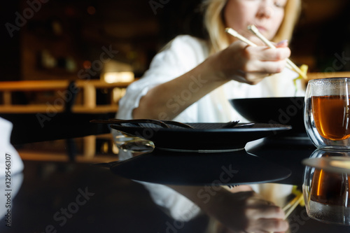 a girl in a Chinese restaurant eats noodles with chopsticks, on a table is a glass cup of teas and lies a smartphone