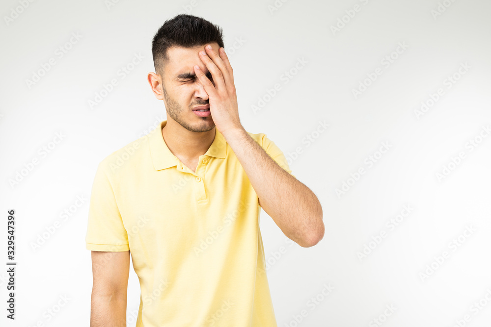 brunette man feels a severe headache and holds his head in his hands on a white studio background brunette man feels a severe headache and holds his head in his hands on a white studio background