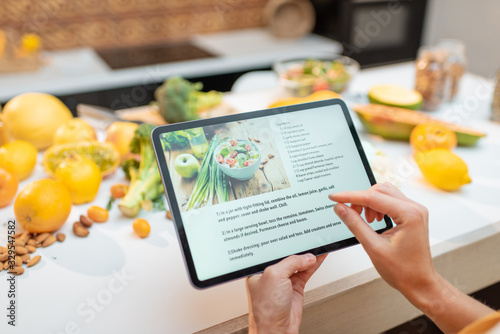 Woman looking on the digital recipe, using touchscreen tablet while cooking healthy meal on the kitchen at home, close-up view on the screen