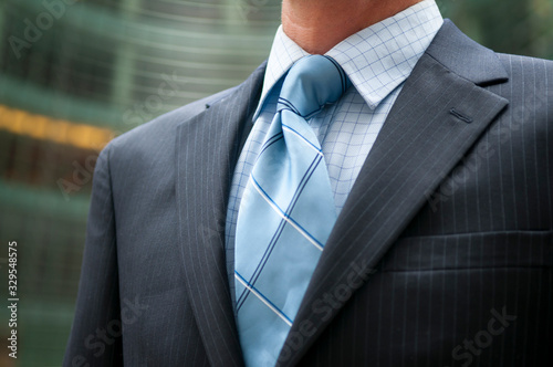 Close-up of unrecognizable businessman in dark pinstripe suit and blue tie standing outdoors in an office building courtyard photo