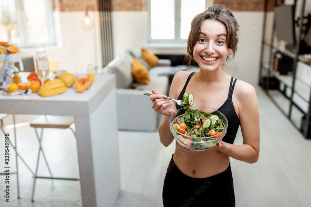 Portrait of a cheerful athletic woman eating healthy salad during a break at home. Concept of losing weight, sports and healthy eating Portrait of a cheerful athletic woman eating healthy salad during a break at home. Concept of losing weight, sports and healthy eating