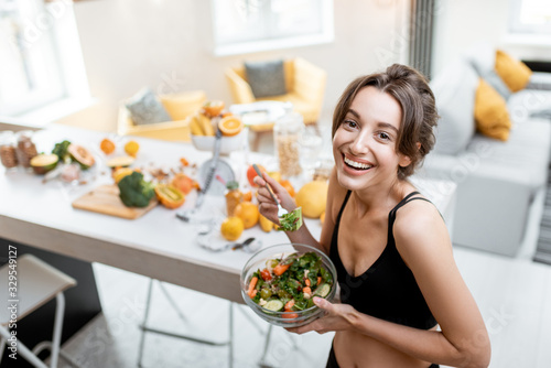 Portrait of a cheerful athletic woman eating healthy salad during a break at home. Concept of losing weight, sports and healthy eating photo