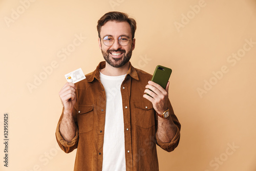 Positive man holding credit card using mobile phone.