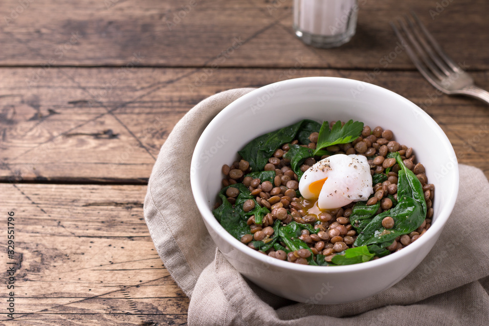 Boiled lentils with spinach, herbs, spices and poached egg in ceramic bowls on wooden background. Simple healthy homemade food Boiled lentils with spinach, herbs, spices and poached egg in ceramic bowls on wooden background. Simple healthy homemade food