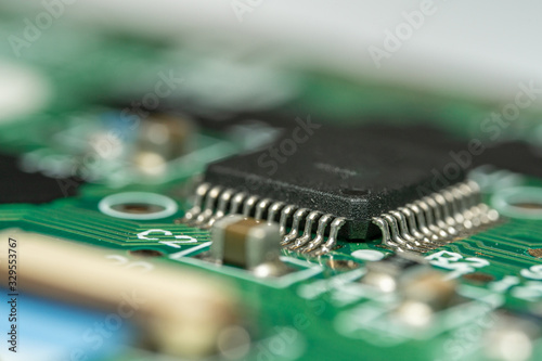 Macro photo with narrow depth of field of an electronic circuit with a microcontroller & components in frame on green electronic board.