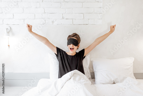 Young woman in sleeping mask waking up in the bedroom. Good morning concept photo