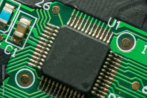 Macro photo of an electronic circuit with a microcontroller & components in frame on green electronic board.