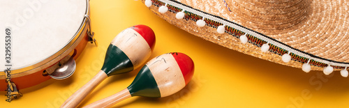Tambourine, maracas and sombrero on yellow background, panoramic shot