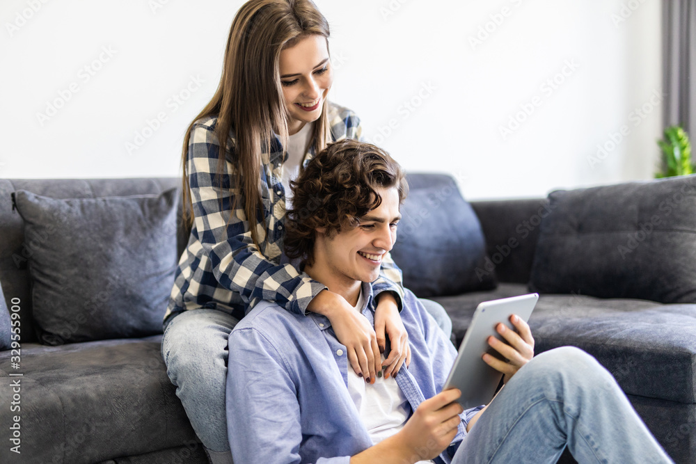 Beautiful couple is using a digital tablet and smiling while sitting on the couch at home