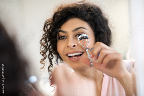Beautiful dark-haired woman curling her eyelashes with a curler