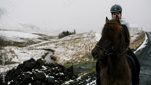 Follow close up of a girl dressed in traditional Icelandic sweater riding her horse around the farm, Iceland