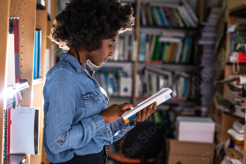 In the campus library, a focused black female student engrosses herself in a book, her surroundings fading as she dives into the world of knowledge and imagination.