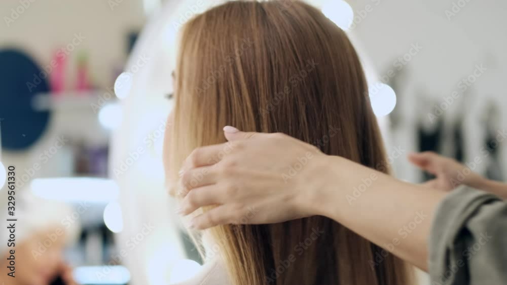 A back view of a professional hairdresser is touching hair of her young blonde woman client at a beauty salon A back view of a professional hairdresser is touching hair of her young blonde woman client at a beauty salon