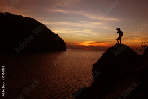 Silhouette of photographer using camera on the top of a rock by the sea , Twilight sky sunset