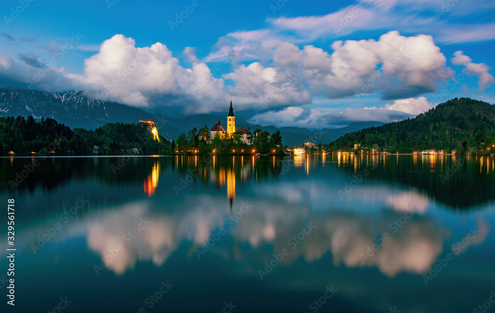 Fototapeta premium Magnificent view of Bled lake and illuminated pilgrimage church on island at twilight reflected in water, Slovenia