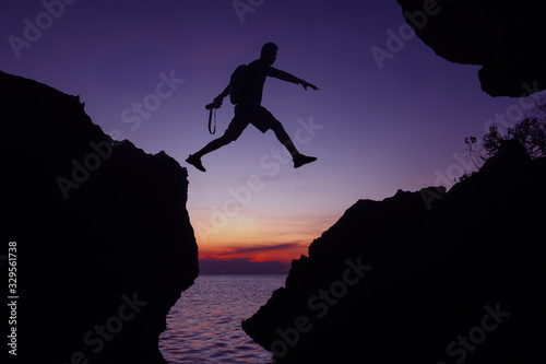 Silhouette of the photographer jumping over the stone at sunset ,Man Jumping between rocks on tropical Sea at twilight sky.