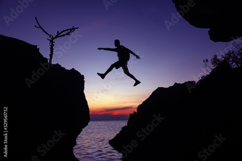 Silhouette of the photographer jumping over the stone at sunset ,Man Jumping between rocks on tropical Sea at twilight sky.