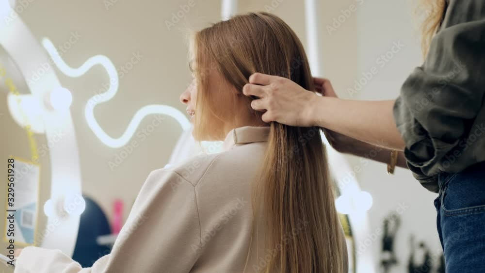 A bottom view of a professional hairdresser is touching long blonde hair of her client at a beauty salon A bottom view of a professional hairdresser is touching long blonde hair of her client at a beauty salon