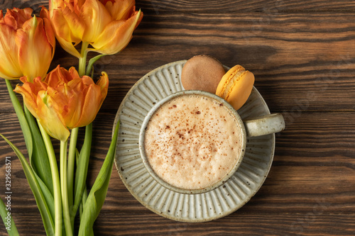 orange tulips, cup with coffee and macaroon cookies on a wooden background, copy space