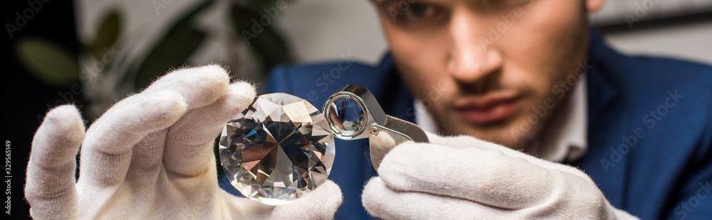 Selective focus of jewelry appraiser examining gemstone with magnifying glass, panoramic shot Selective focus of jewelry appraiser examining gemstone with magnifying glass, panoramic shot