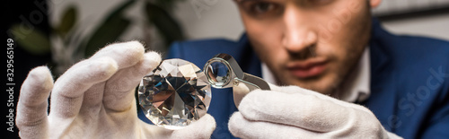 Selective focus of jewelry appraiser examining gemstone with magnifying glass, panoramic shot photo