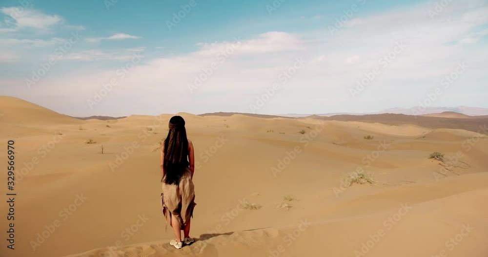 Anonymous woman stands over sand dunes in endless desert Pan shot from behind of a single girl stands alone looking away to unlimited eyesight all covered by sands Anonymous woman stands over sand dunes in endless desert Pan shot from behind of a single girl stands alone looking away to unlimited eyesight all covered by sands