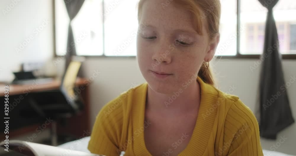 Bored little girl in bedroom at home flipping through book pages. Lone redhead female child sitting on bed with emotions, feelings of boredom and loneliness Bored little girl in bedroom at home flipping through book pages. Lone redhead female child sitting on bed with emotions, feelings of boredom and loneliness