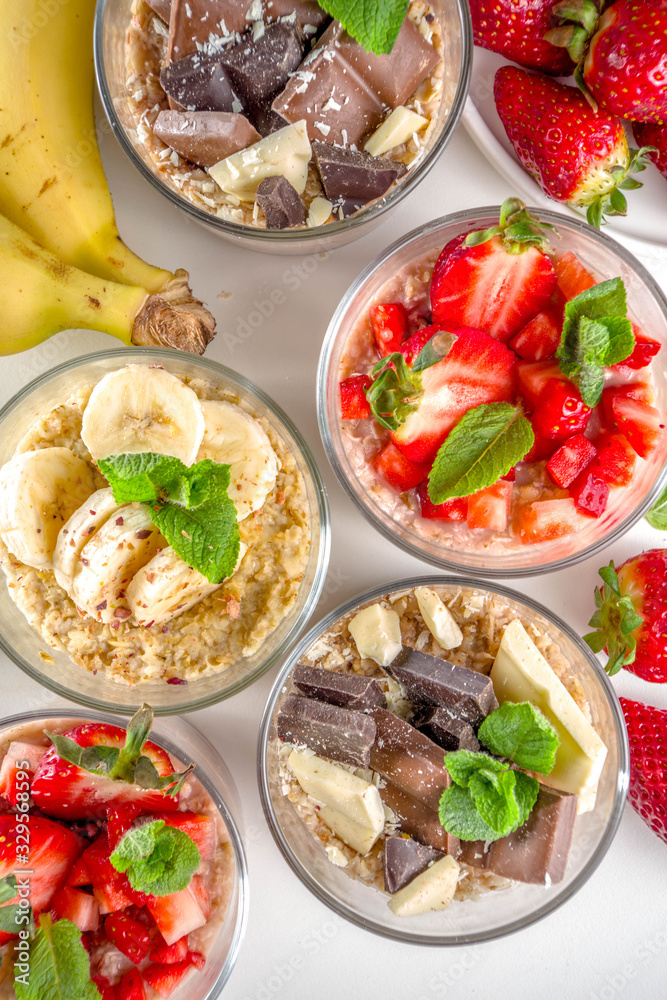 Set various fruit overnight oatmeal. Oats porridge with strawberry, bananas, chocolate, nuts in small portion jars. Summer breakfast oatmeal. Healthy vegan diet snack.