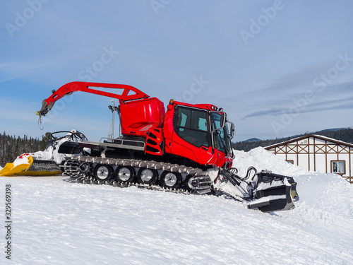 A red snowcat at a ski resort is preparing to tamp the snow. Winter sunny day