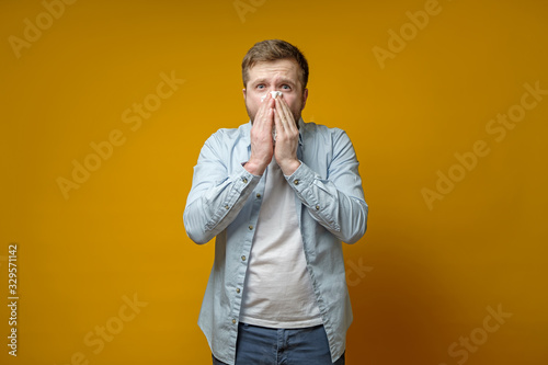 Man caught a cold and has a runny nose, he uses a handkerchief and looks scared at the camera. Concept of the spread of the virus.