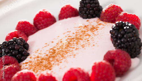 raspberries and blackberries laid out on a white plate in circle with yogurt and cinnamon