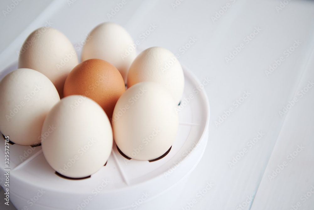 Chicken eggs in a egg electric cooker on a white wooden table Chicken eggs in a egg electric cooker on a white wooden table