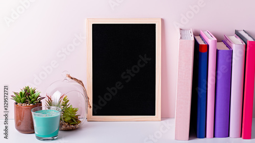 Bookshelf with multicolor books, house plants succulents and black board frame for text. Background for World Book Day. Still life with stack of colorful books and chalkboard