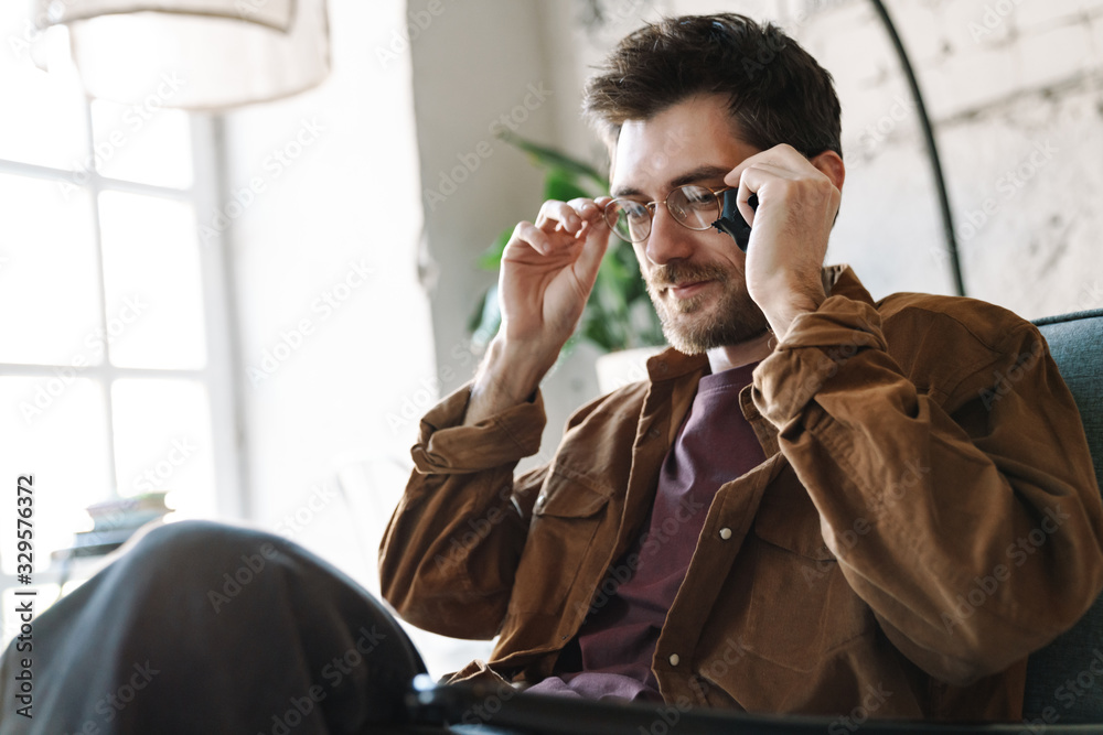 Fototapeta premium Image of unshaven young man holding eyeglasses while resting in cafe