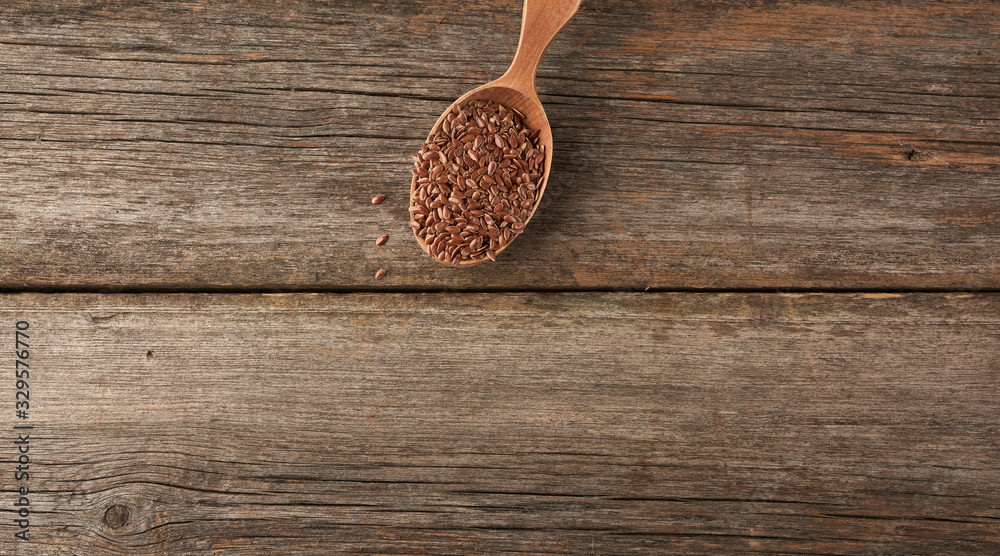 dry brown flax seeds in a brown wooden spoon on a gray wooden table from old boards, top view
