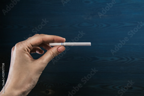 Cigarette in a female hand on a wooden background in a blue haze copy space. Female smoking.