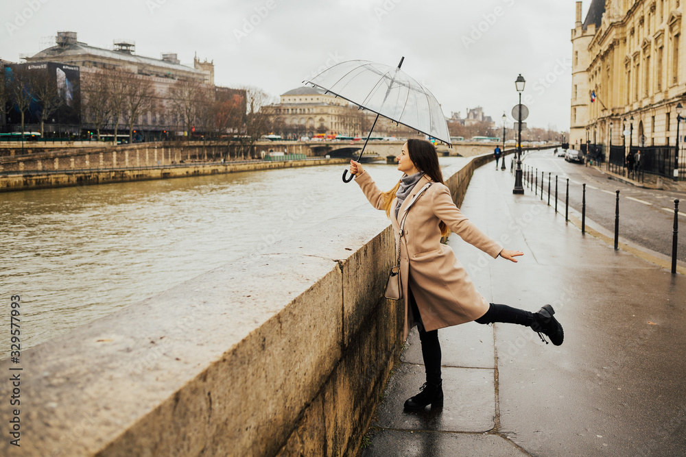 Happy young girl admiring French architecture from Pont au Change, historic bridge known for trade by money lenders, jewelers and goldsmiths. She dressed in a beige coat and hold in hand umbrella.