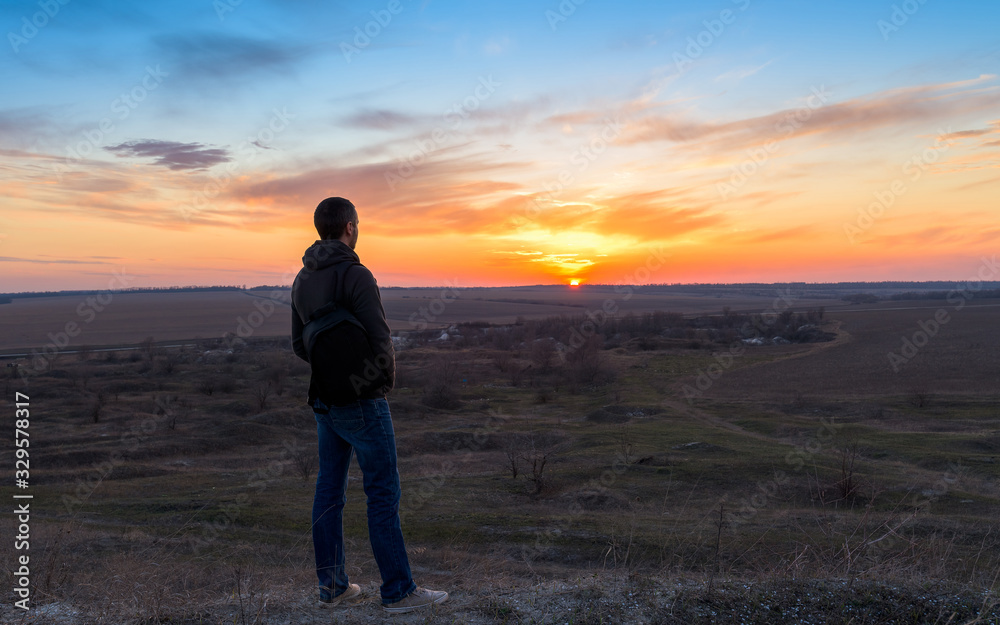 a man with a backpack at sunset stands on a mountain, looking at the sun. freedom of movement. trekking on top of a mountain. wild life in nature. camping.