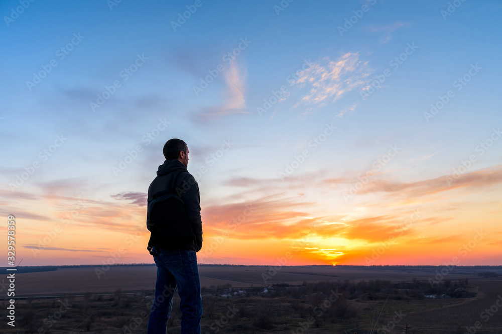 a man with a backpack at sunset stands on a mountain, looking at the sun. freedom of movement. trekking on top of a mountain. wild life in nature. camping.