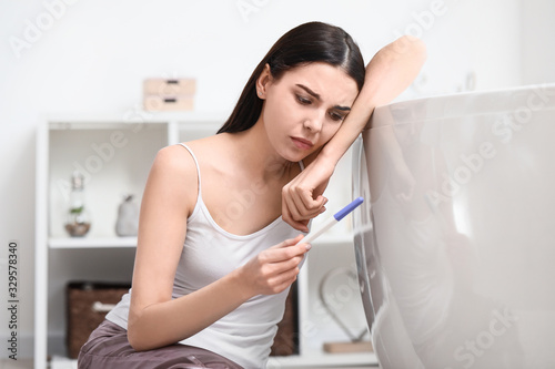 Sad young woman with pregnancy test in bathroom