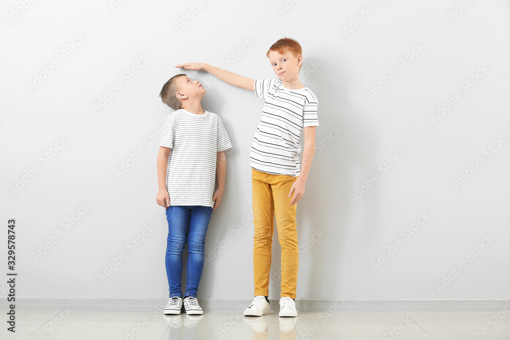 Cute little boys measuring height near light wall Cute little boys measuring height near light wall